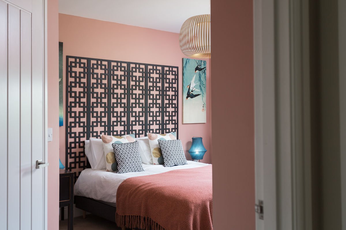 glimpse through bedroom door into pink bedroom with art deco headboard