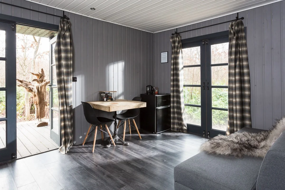 holiday home living space with grey wooden walls, dark wooden flooring, small breakfast table, grey sofa