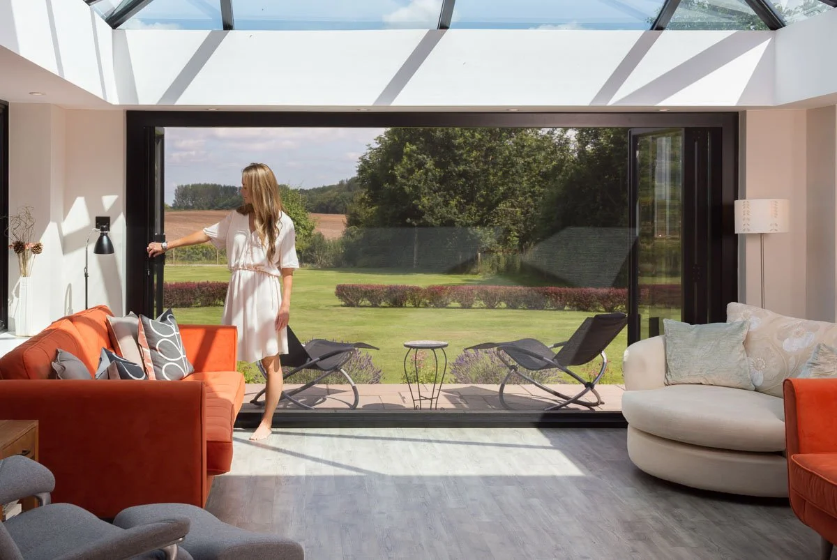 inside garden room with bifold doors, lady with white dress sliding open almost shut bug screen