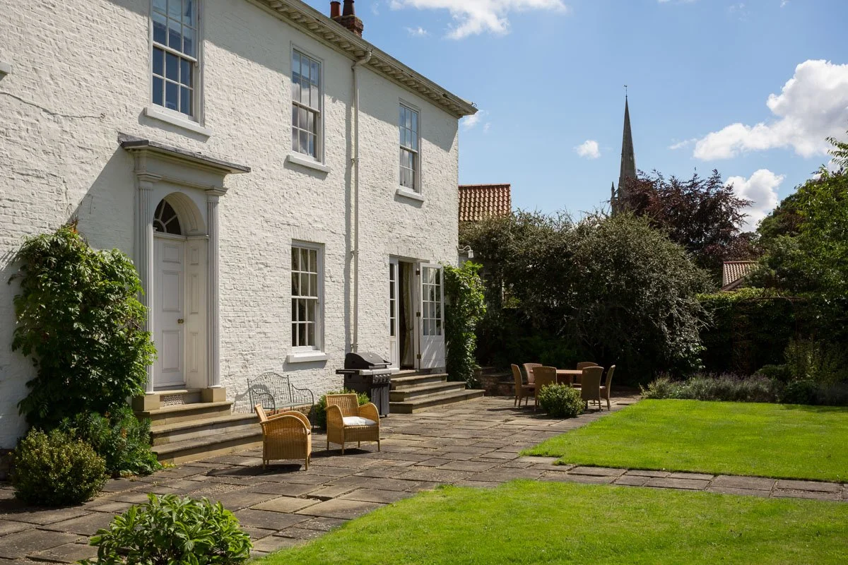 large white Georgian house with flagstone patio and wicker furniture and manicured lawn