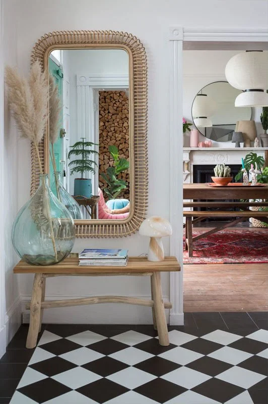 one point perspective of hallway wall with wood bench table, gold framed mirror, pampas grass, black and white tile check flooring and a glimpse into the dining room beyond