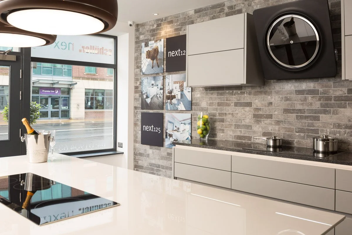 detail shot of kitchen showroom looking across white counter top towards cooker and gallery wall