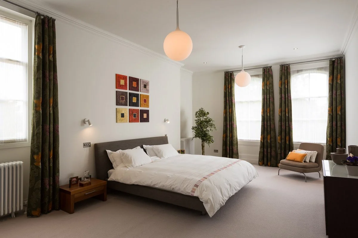 large bedroom with pendant lights, white walls, dark grey bed, beige carpet, large sash windows