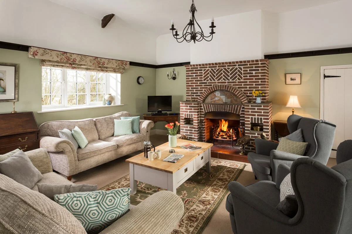 large living room, sage green walls, beige sofas, grey armchairs and brick surround fireplace