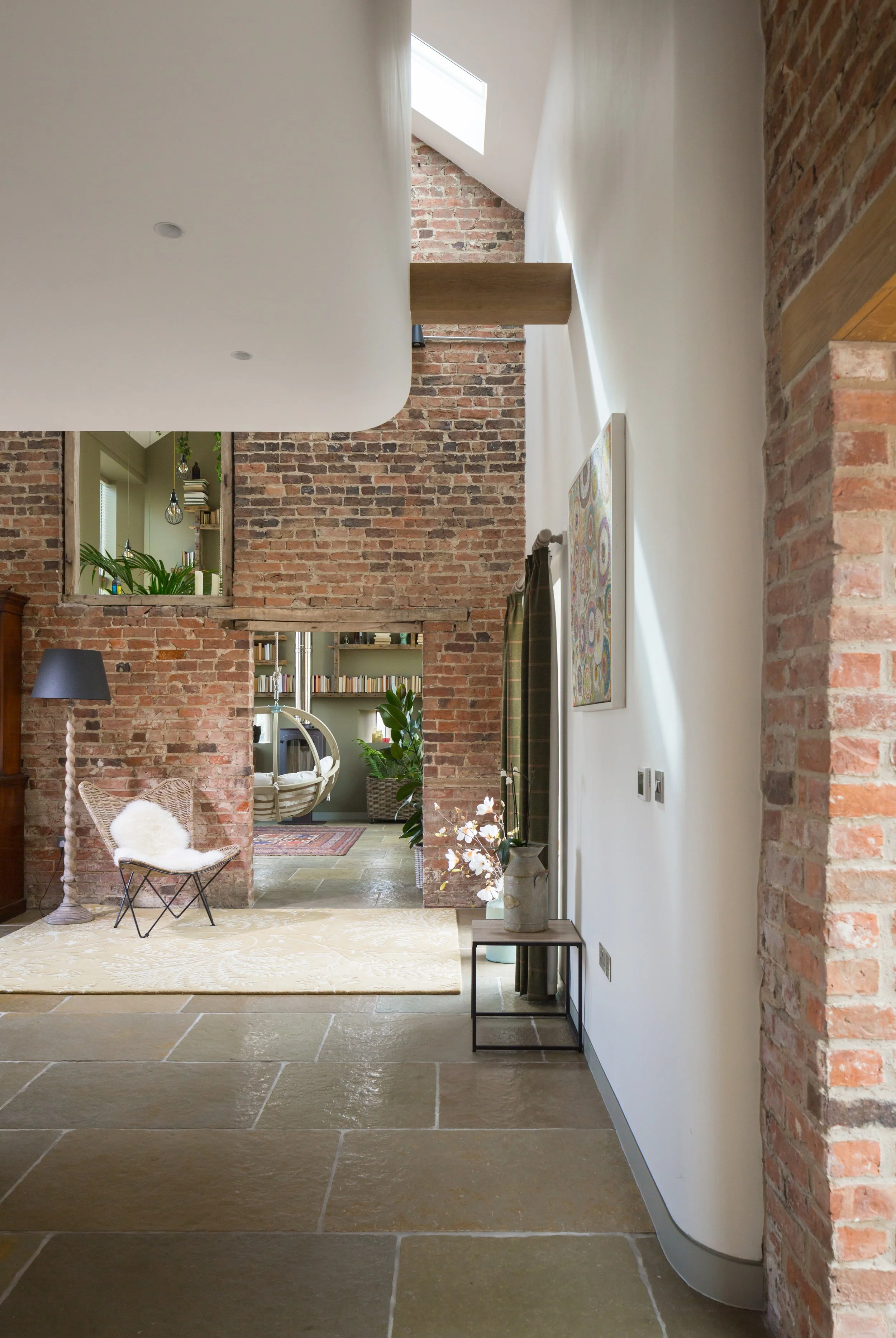 Double height space interior with exposed brick, plaster, skylight and view through to hanging chair