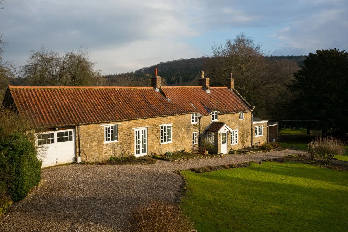 old farmhouse with long driveway and lawn surrounded by trees