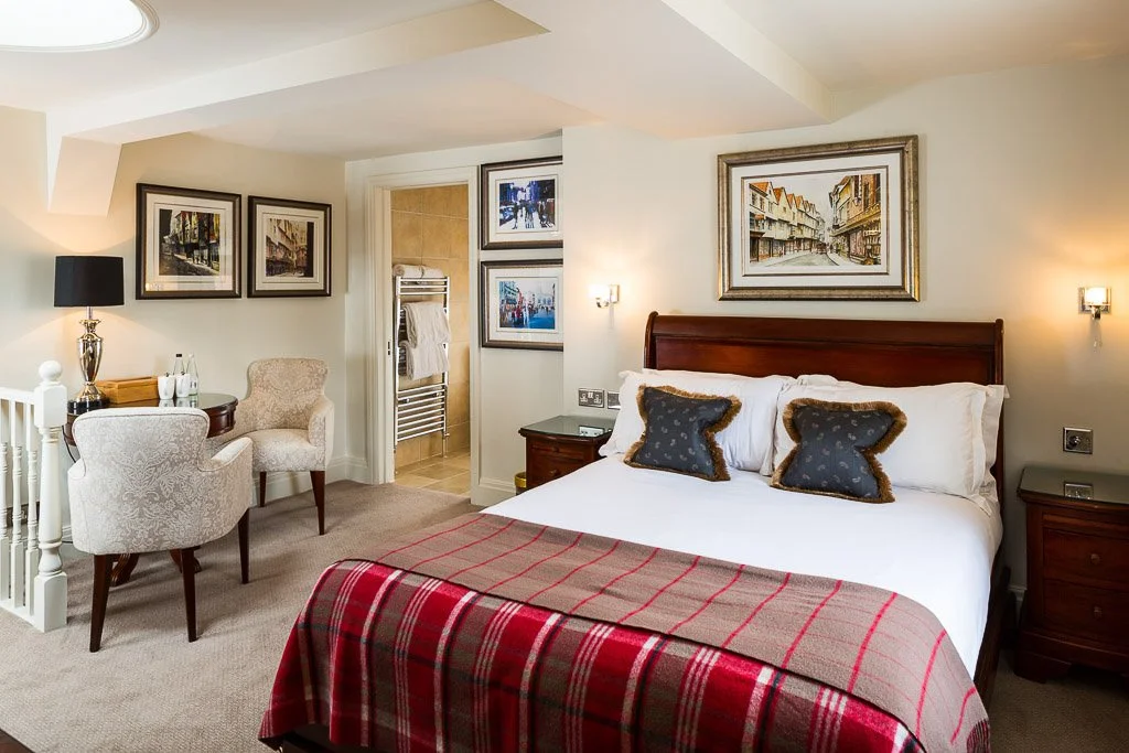 large bedroom with deep wooden bed and a glimpse into en-suite beyond