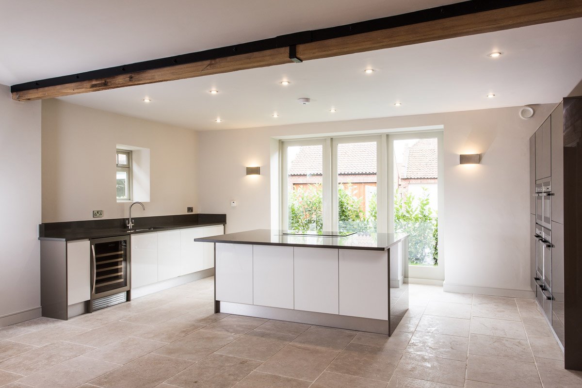 large kitchen with beige tile flooring, white units, dark countertops and island