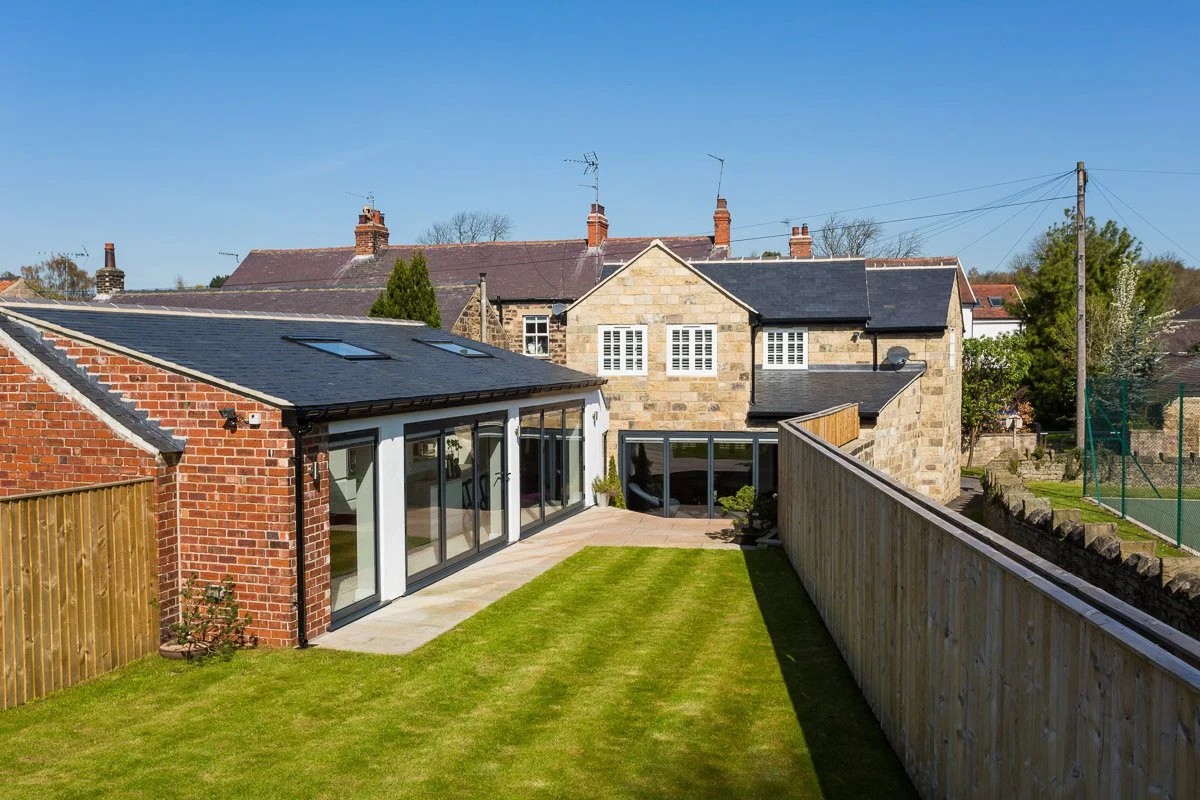 elevated rear shot of renovated cottage with bifold doors, patio area and manicured lawn