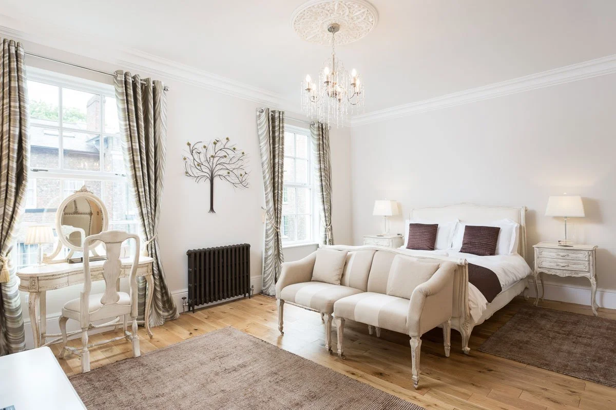 large bedroom with sash windows, wooden flooring, bench seat at end of bed