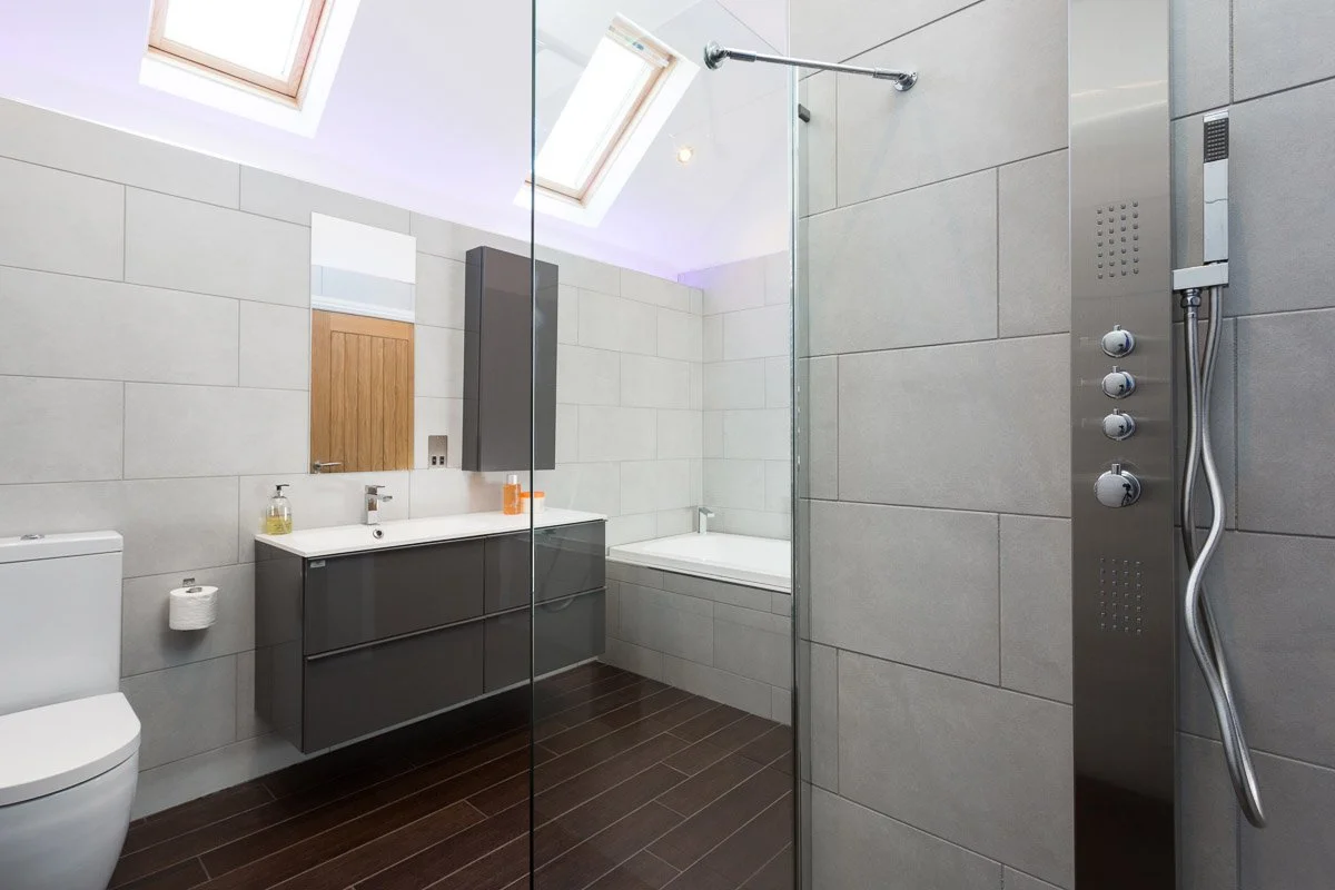 modern bathroom with dark wooden flooring, pale tile walls and skylights