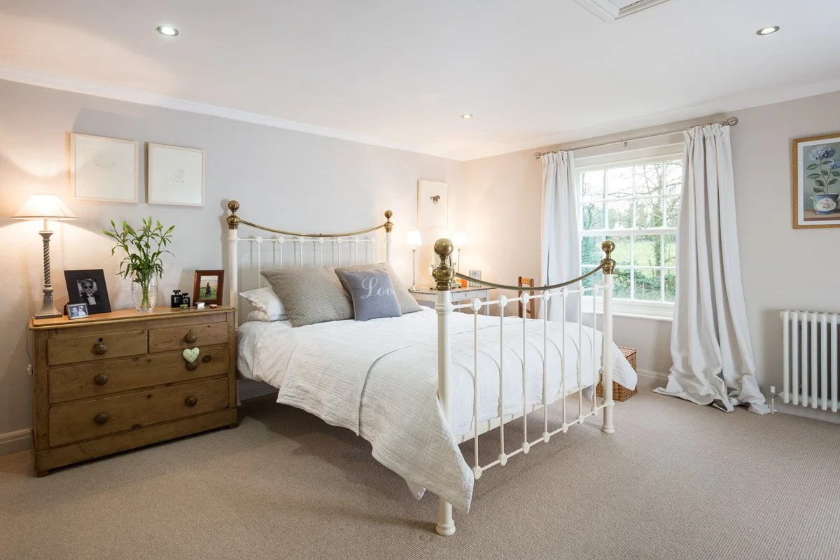 large bedroom with tall metal frame bed, pale grey walls, beige carpet, white bedding 