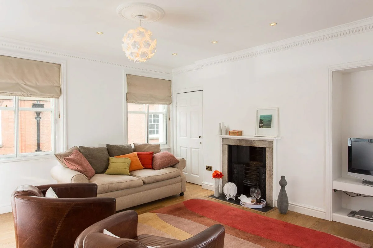 living room with white walls, wooden flooring, two brown leather armchairs, beige sofa and fireplace
