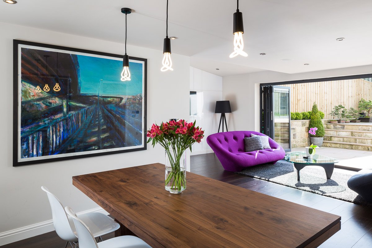 large dining/family room with dark wooden dining table, bright purple sofa and bifold doors