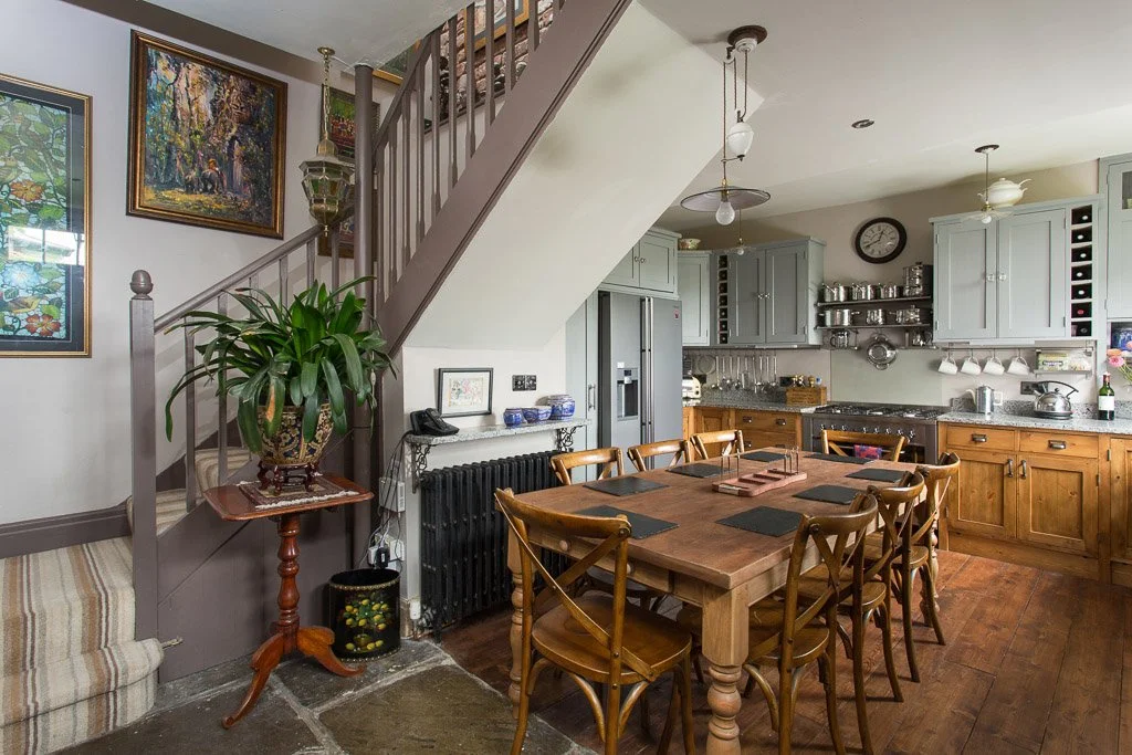 country style kitchen with large wooden dining table, half wooden half flagstone flooring wooden units and staircase leading above