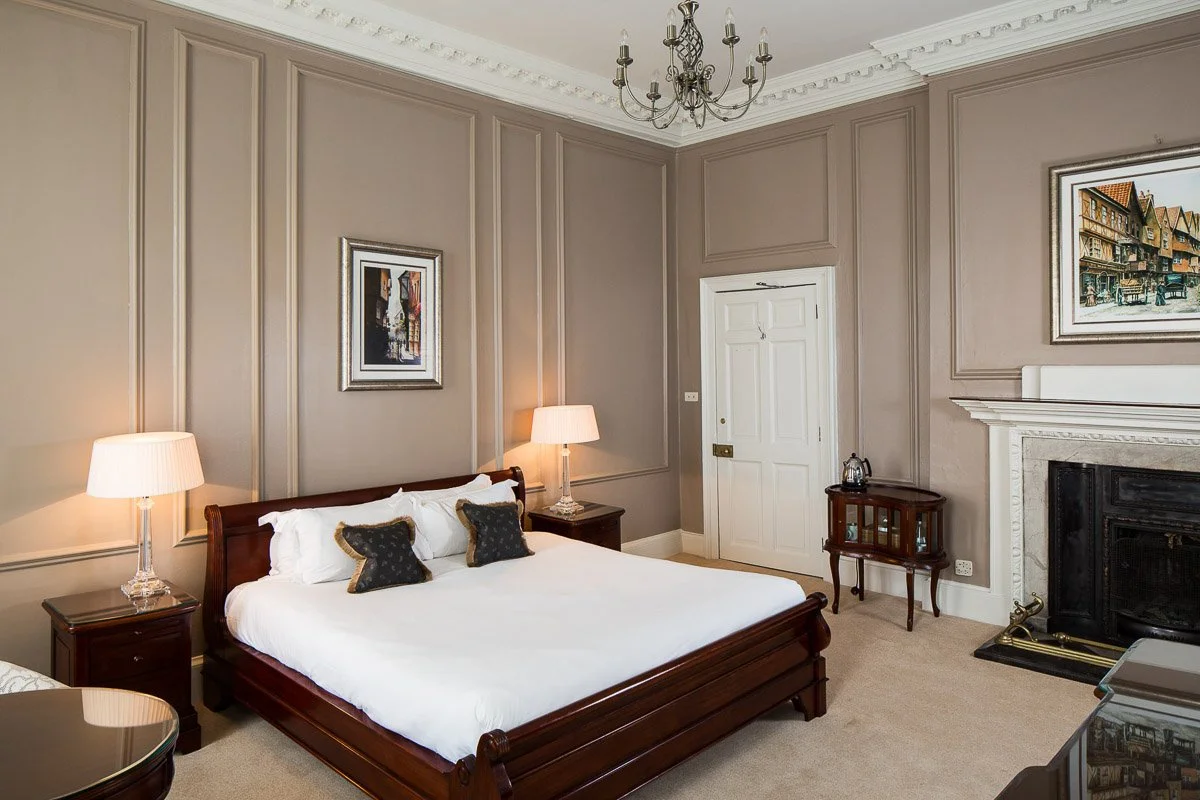 large hotel room with high ceilings, pale pink magnolia walls, large dark wooden bed and traditional fireplace