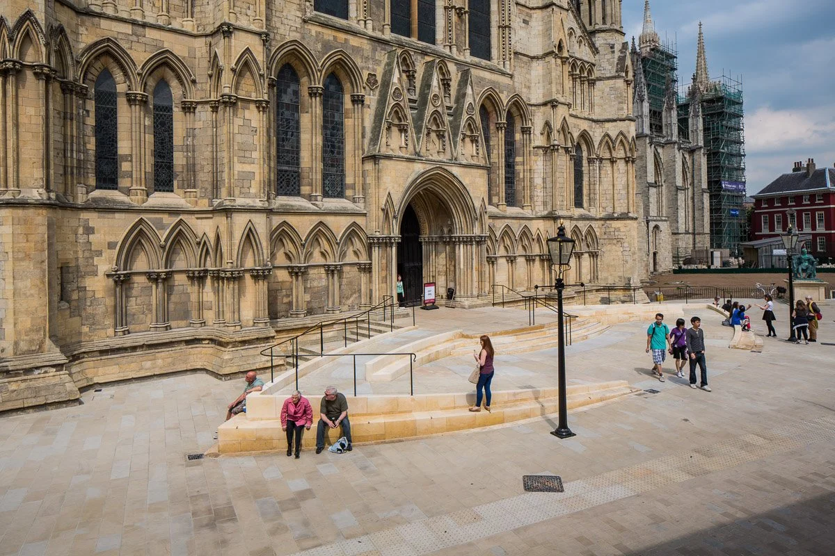 elevated image of the south doors of york mister with new stairs and ramp leading to the doors, people sat and walking across the new piazza 