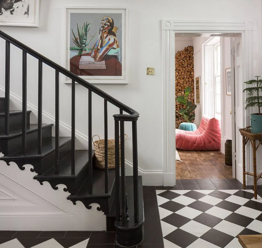one point perspective of hallway with black and white check tile floor, black staircase, glimpse into living room 