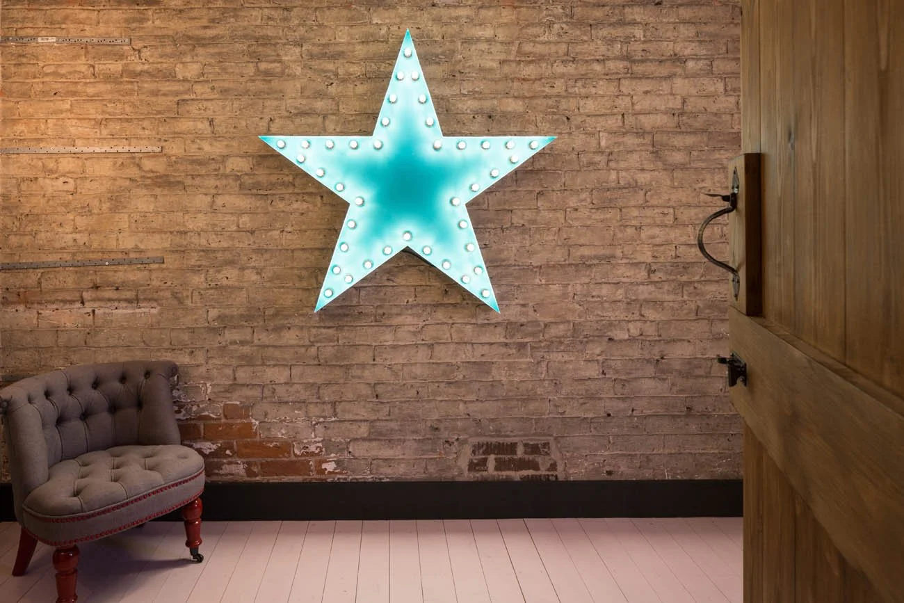brick wall with pale blue light up star, small fabric arm chair and wooden latched door