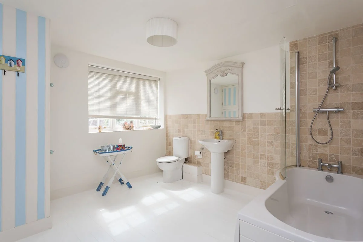 large bathroom tile flooring, beige tile walls, blue and white striped wall on left, sash window
