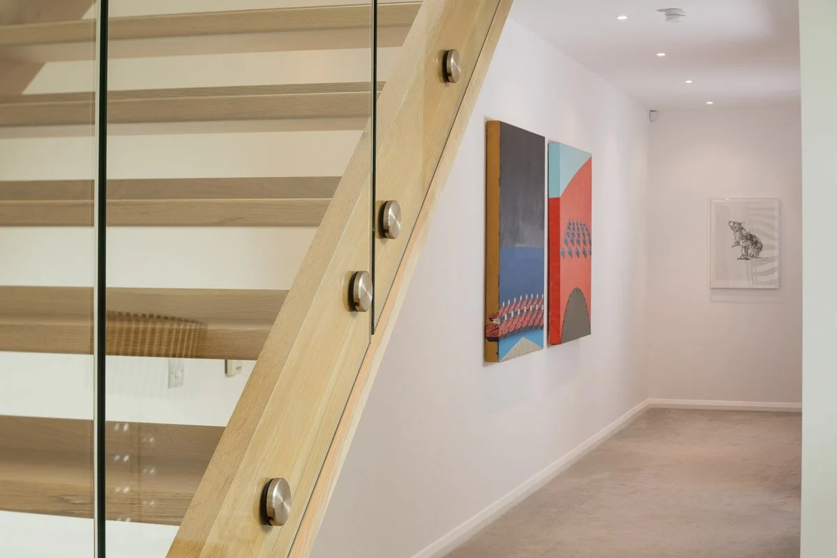 detail image of wooden stair case with glass banister hallway with art behind