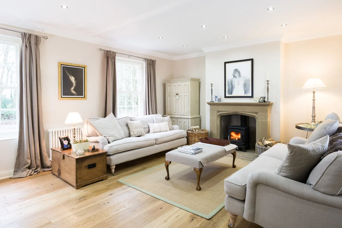 large living room with white walls, wooden flooring, fire place with log burner, cream sofas  