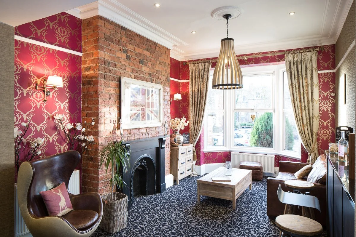 hotel lounge with red wall paper, large leather chairs, black carpet and traditional fireplace