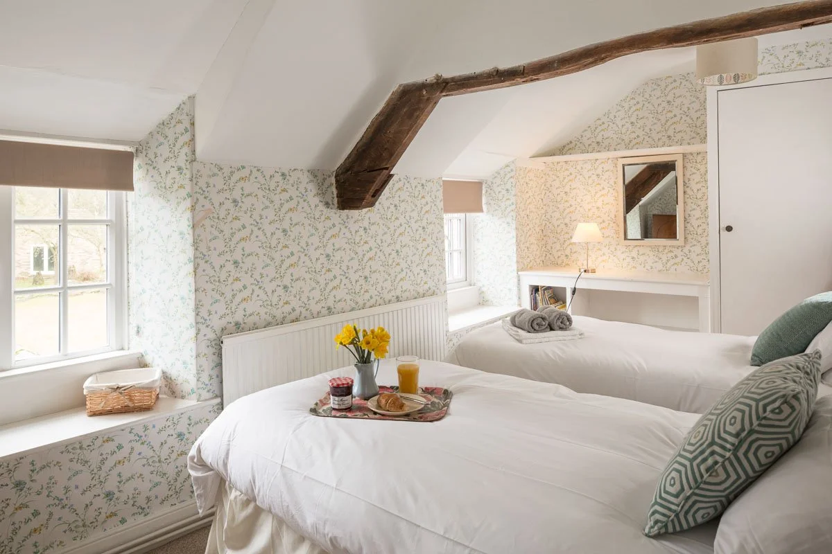small bedroom with lofted ceilings, sage green patterned wallpaper, breakfast trays on bed