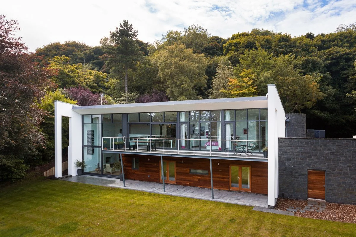architect design house living room with full height glass wall, surrounded by trees and manicured lawn to front