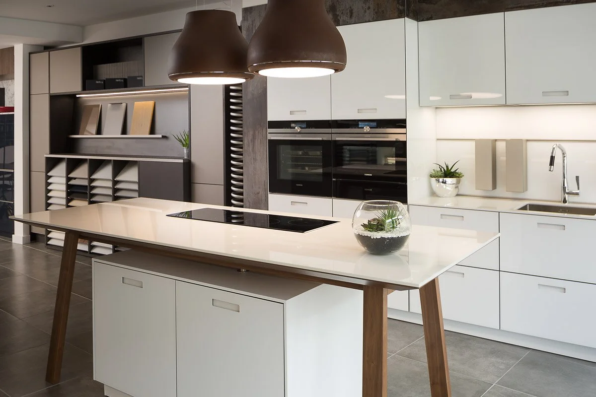 detail shot of kitchen showroom looking across white counter top towards ovens and materials wall