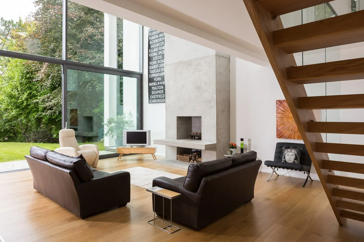 architect design house living room with full height glass wall, modern polished concrete fireplace, leather sofas and wooden staircase
