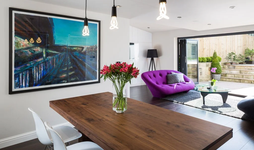 large dining/family room with dark wooden dining table, bright purple sofa and bifold doors
