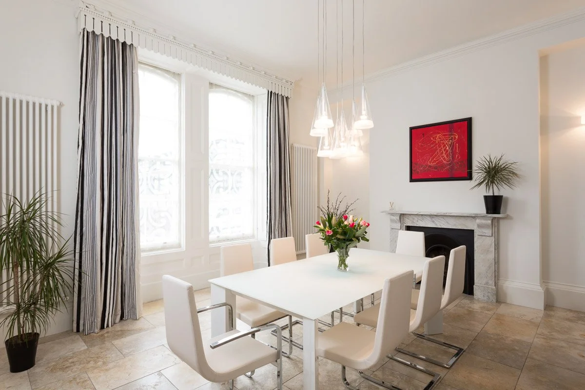 high ceiling dining room with white walls, beige tile flooring, white dining table with white chairs 