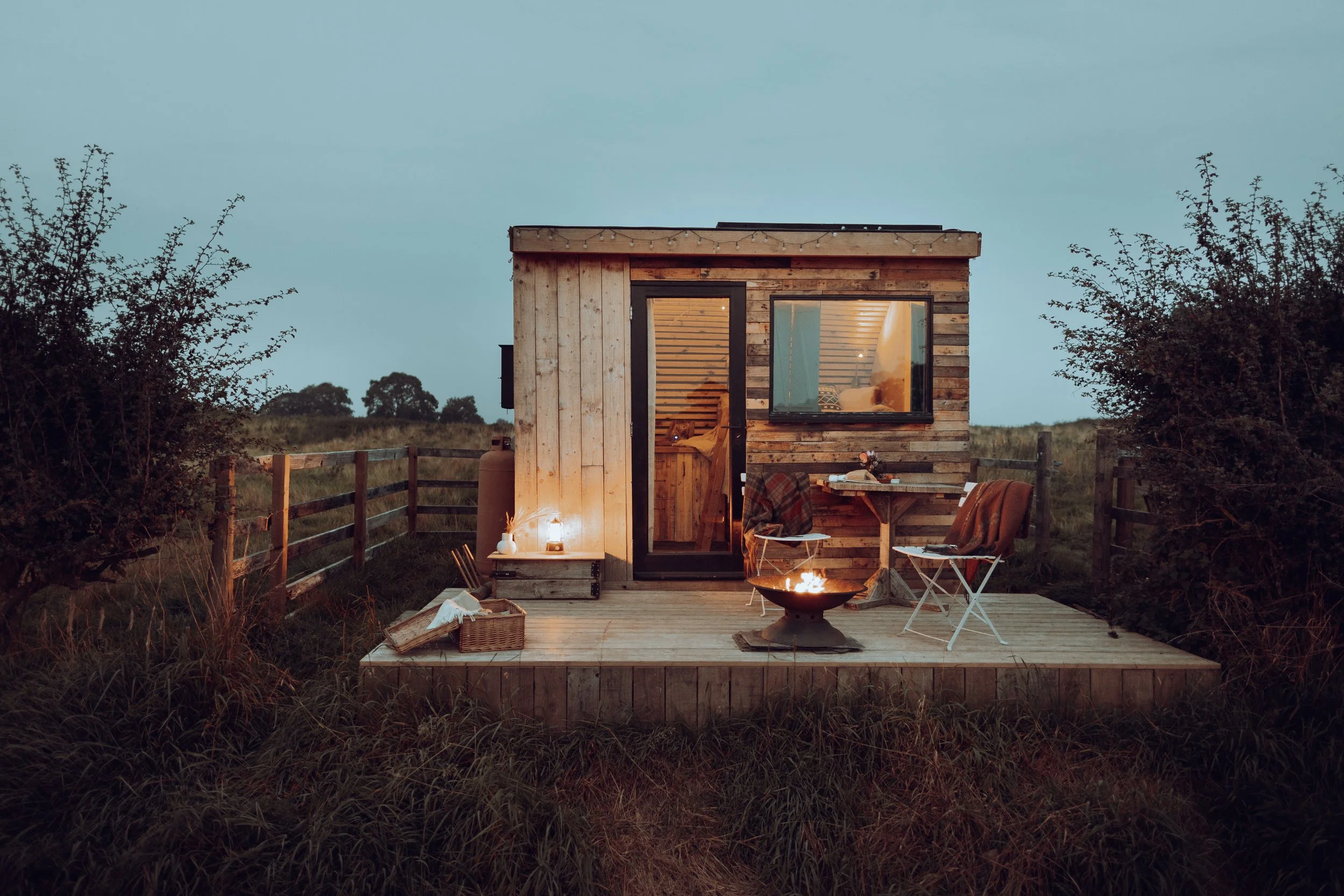 Photograph of a glamping pod at twilight  with a firepit and timber deck