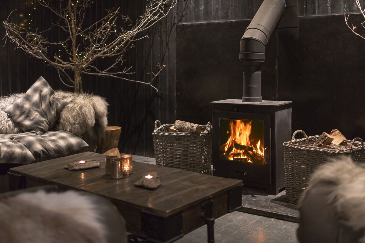 detail shot of cabin living area with cosy chairs and sheepskins, large coffee table and lit log burner