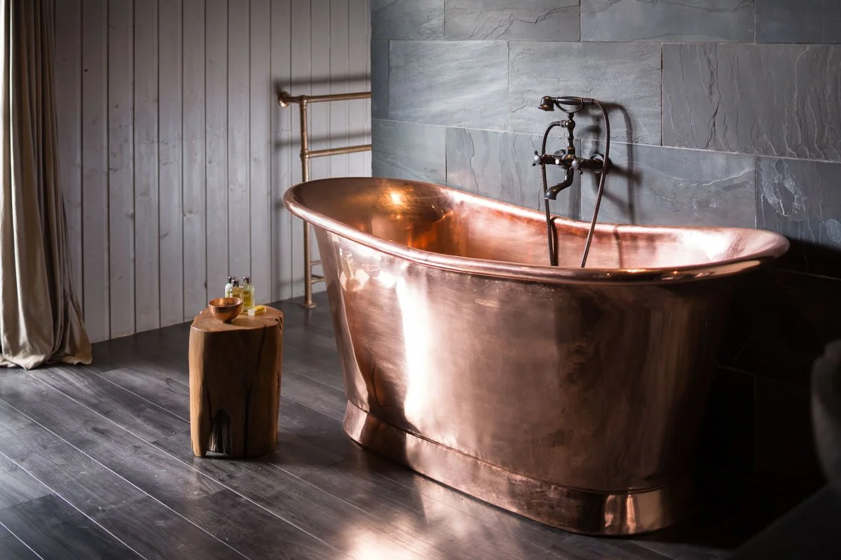 Copper bathtub against a dark slate tile wall