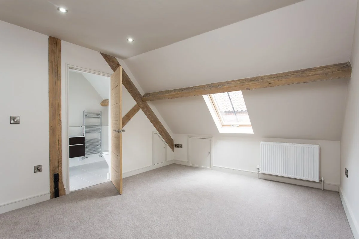 lofted ceiling carpeted bedroom with wooden beams, looking through to en-suite 