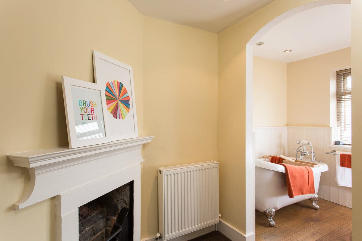 bathroom with powder yellow walls, traditional fireplace, large curved freestanding bath