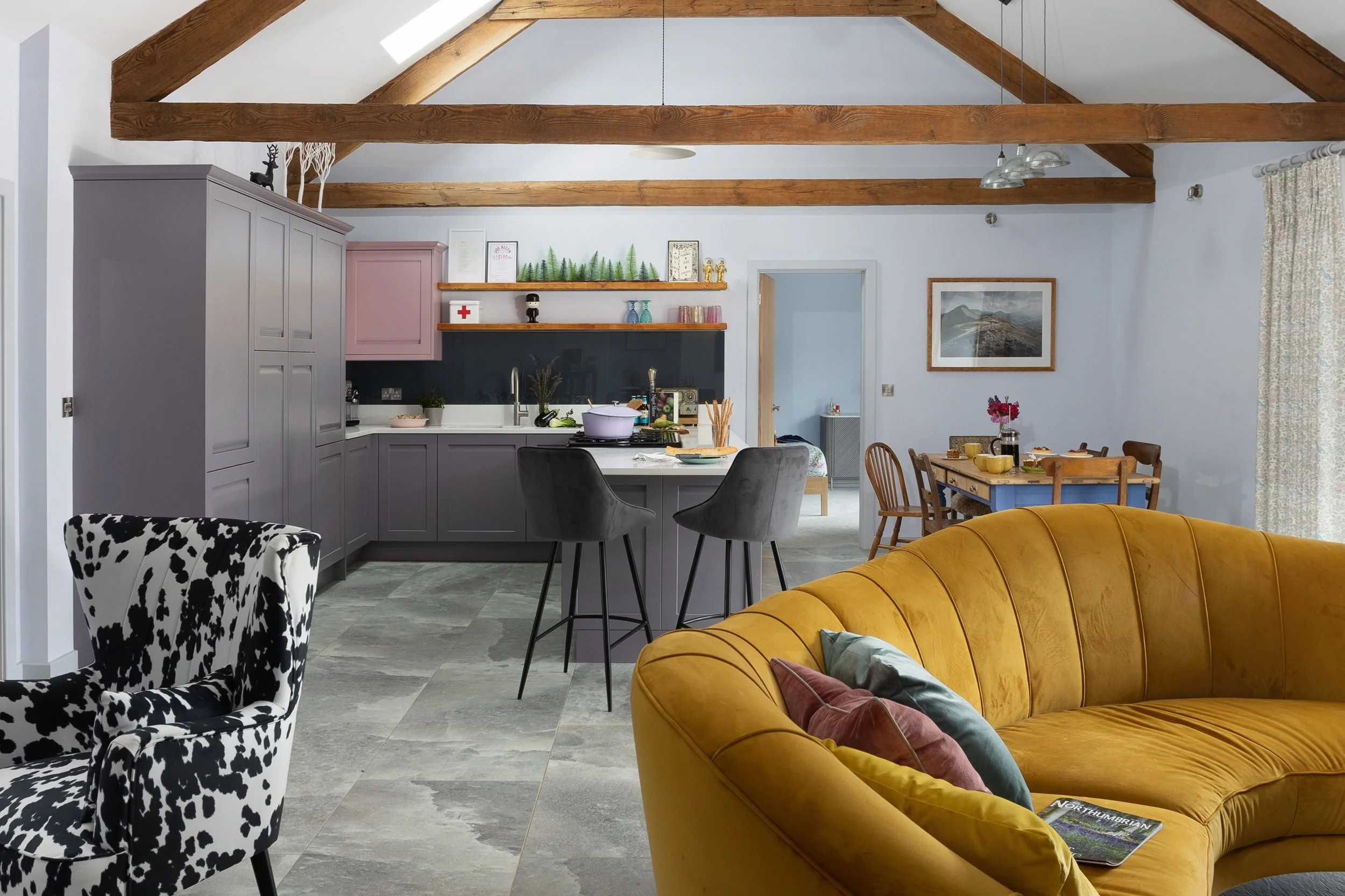 lofted beamed ceiling large kitchen diner with dark grey units, cow print arm chair and yellow sofa