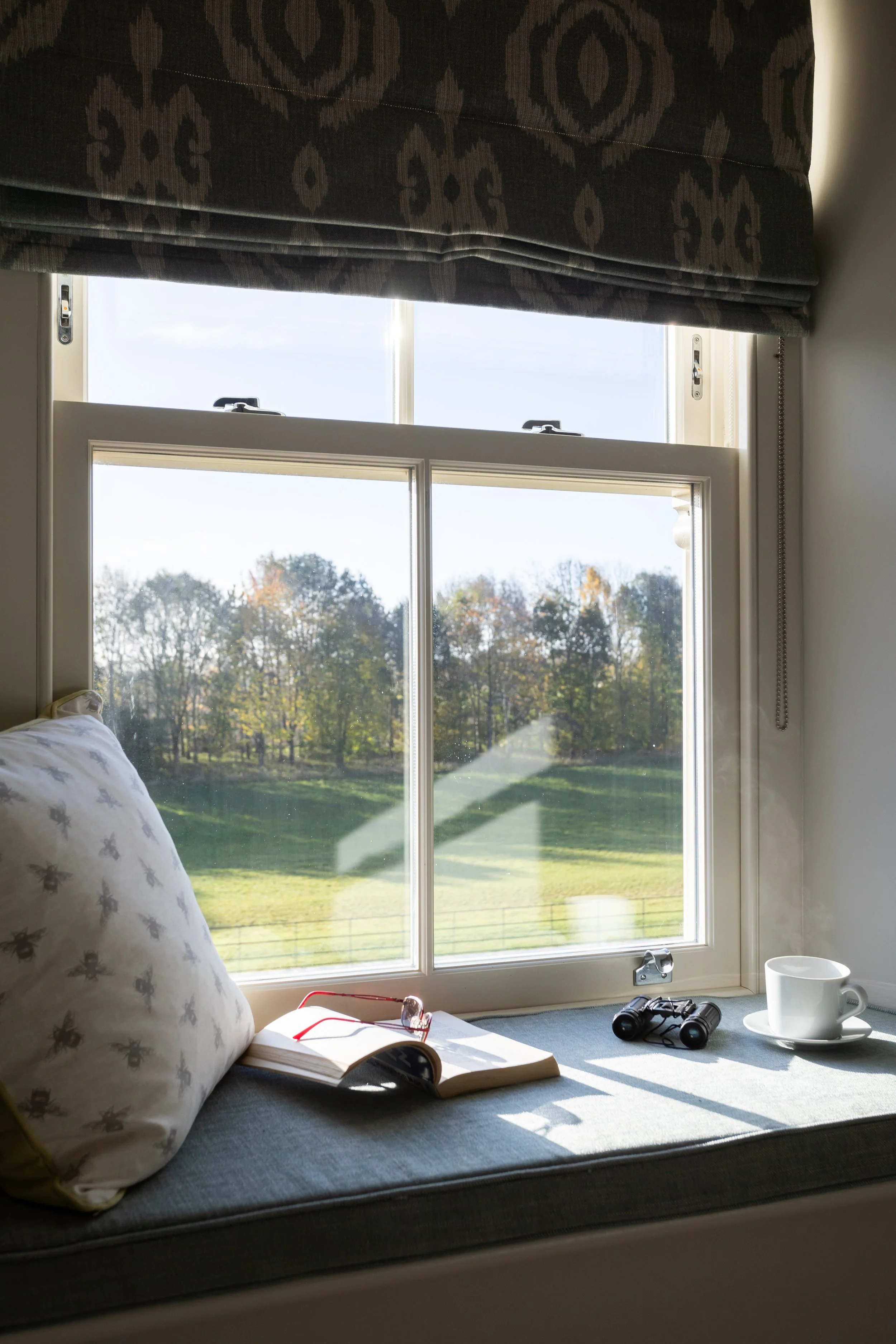 Windowsill with sash frame window, book, cup of steaming coffee and a view to parkland
