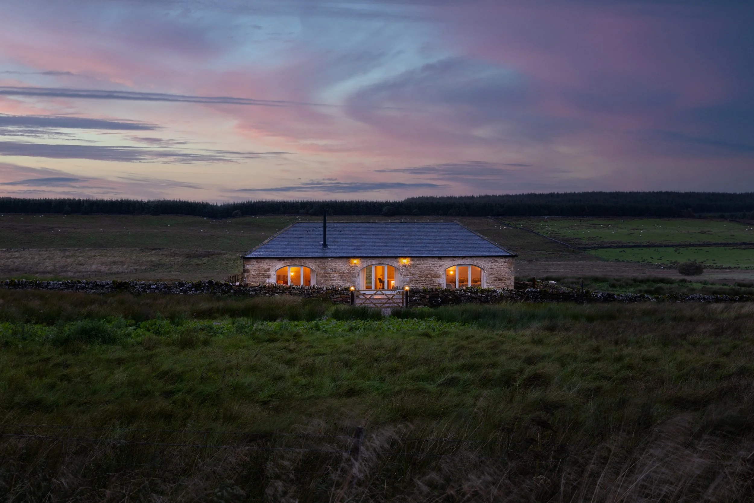 small stone cottage at dusk surrounded by moorland with glowing windows