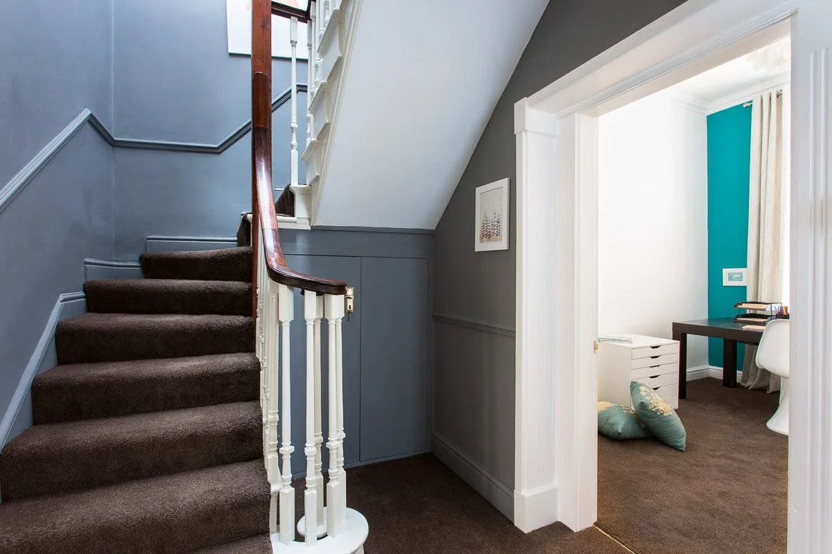 staircase leading up with powder blue walls, looking through doorway to bedroom with bright teal wall, brown carpet and white draw unit