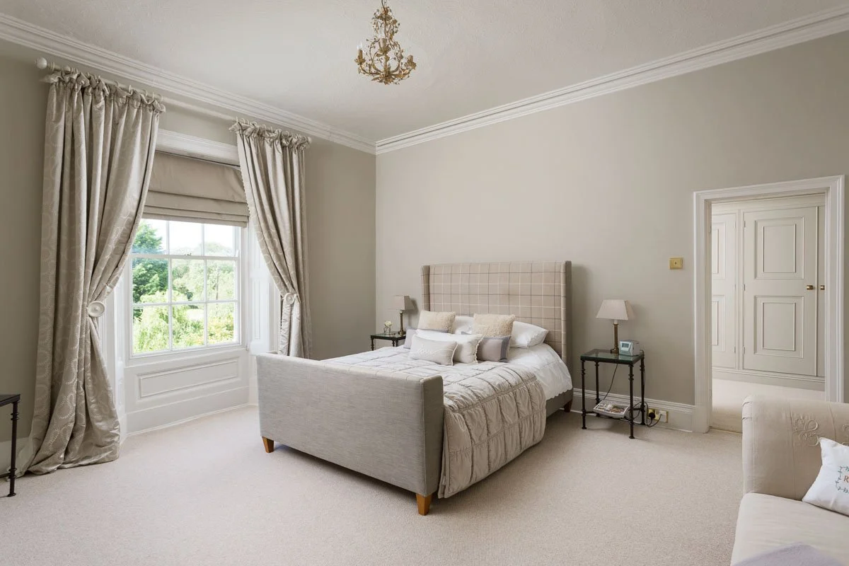 large high ceiling bedroom with beige walls, sash window, beige bed