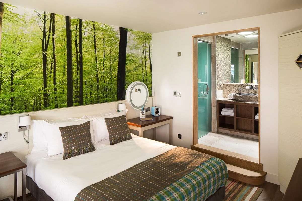 hotel room with woodland scene print above bed, looking through to en-suite