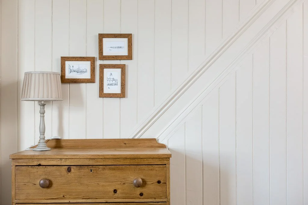 white wood panelled wall with light wooden dresser and lamp 
