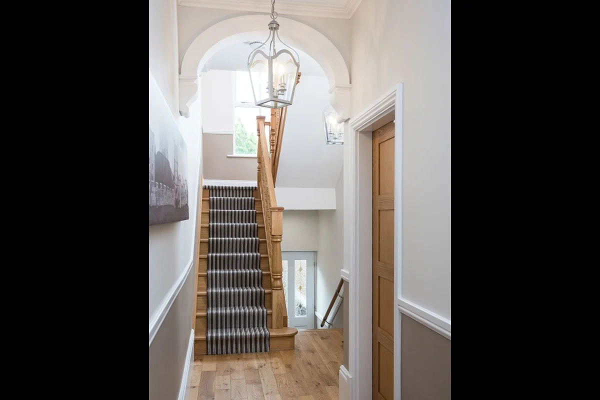 portrait of landing, stairs going up and down, wooden flooring, carpet runner up centre of stairs, large sash window on second landing 