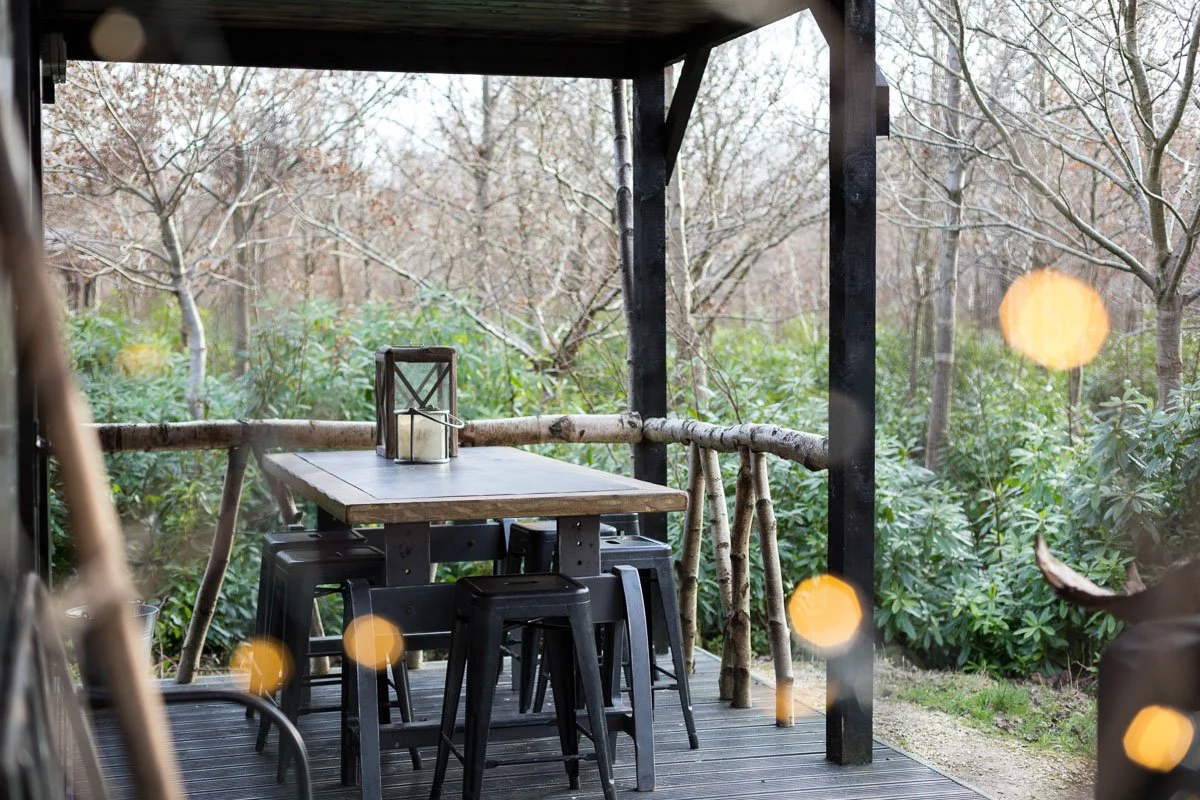decking area with wooden table and metal stools, fairy lights blurred in foreground