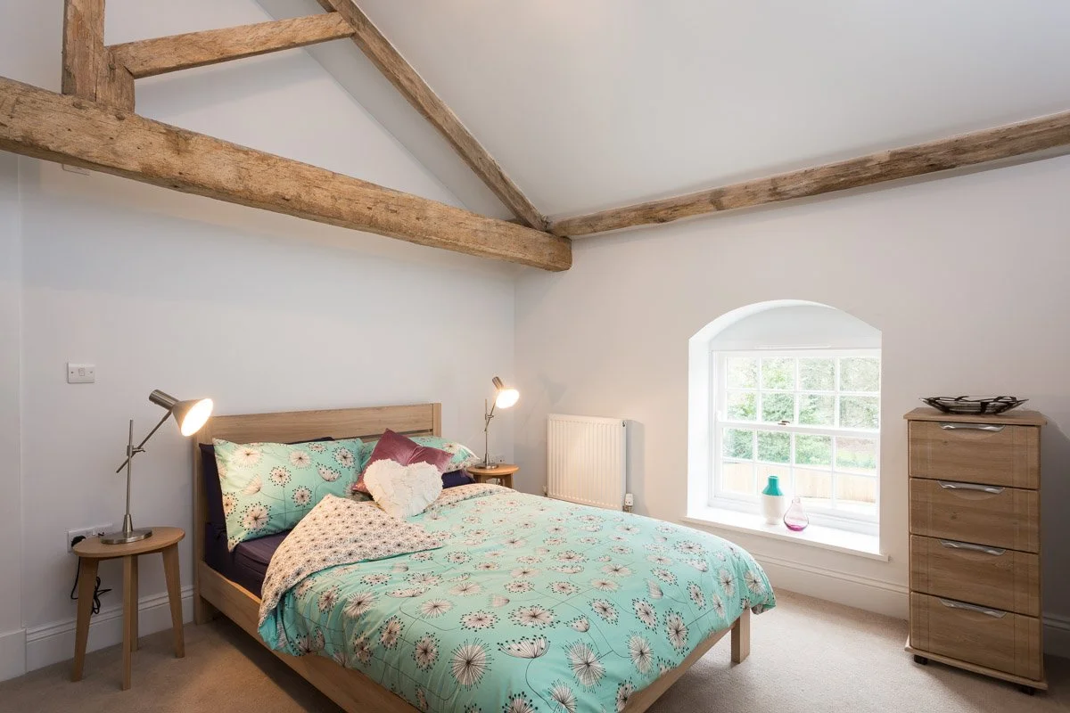 high beamed ceiling bedroom with teal bedding bed, beige carpets, wooden draw unit