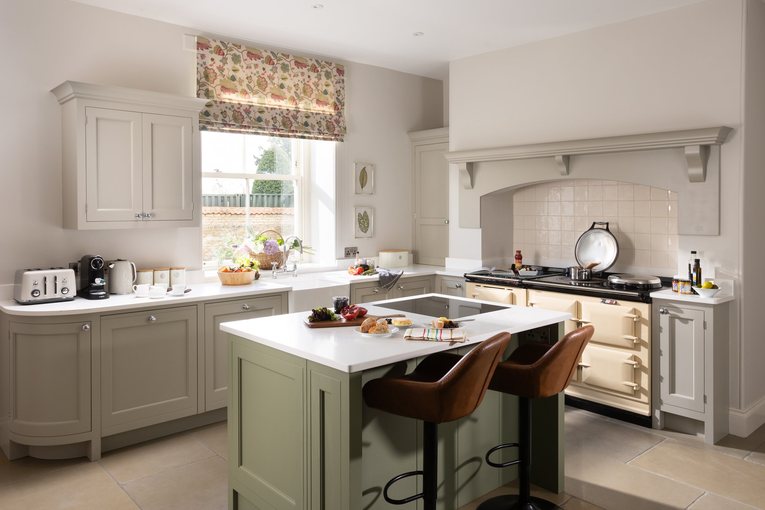A grey painted in-frame country kitchen with cream AGA, green island, belfast sink and induction hob. 