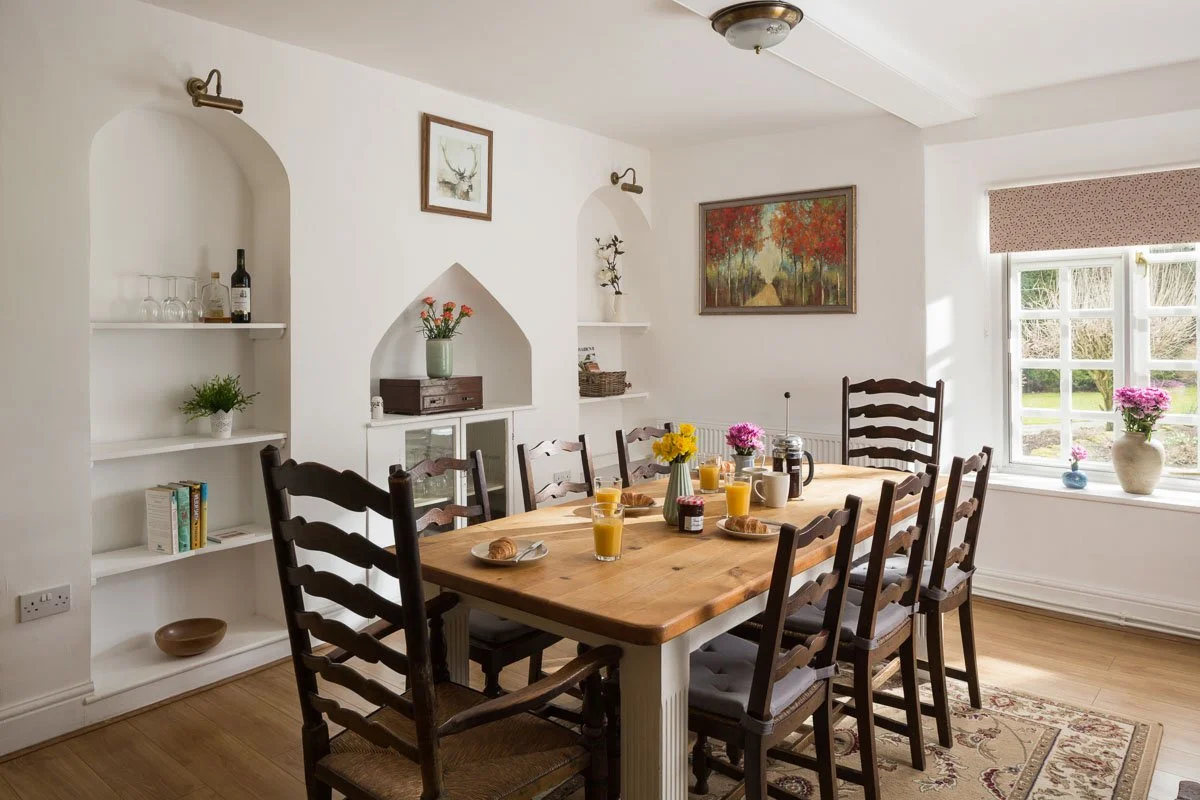 spacious dining room with white walls, wooden flooring, large wooden dining table, shelved alcoves in wall